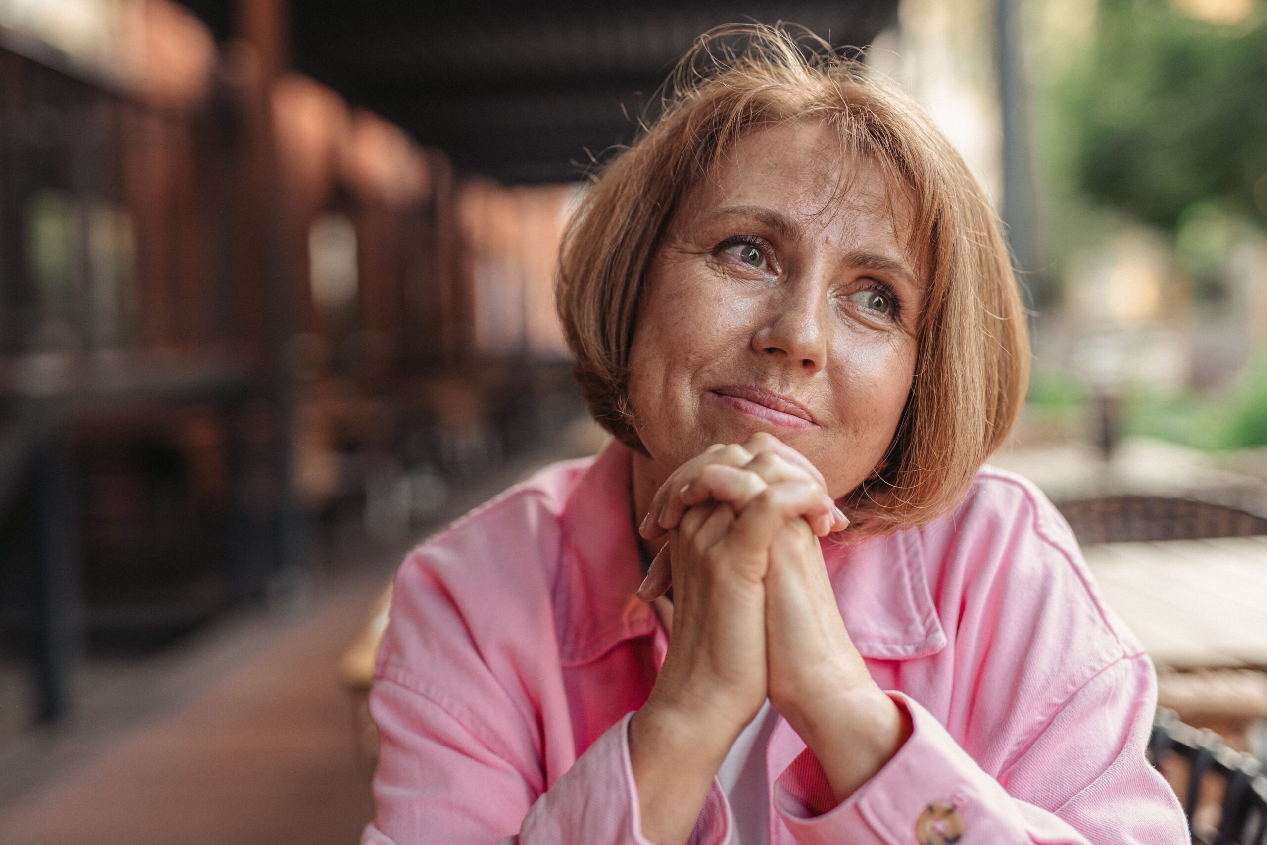 Thoughtful woman in pink clasps hands.