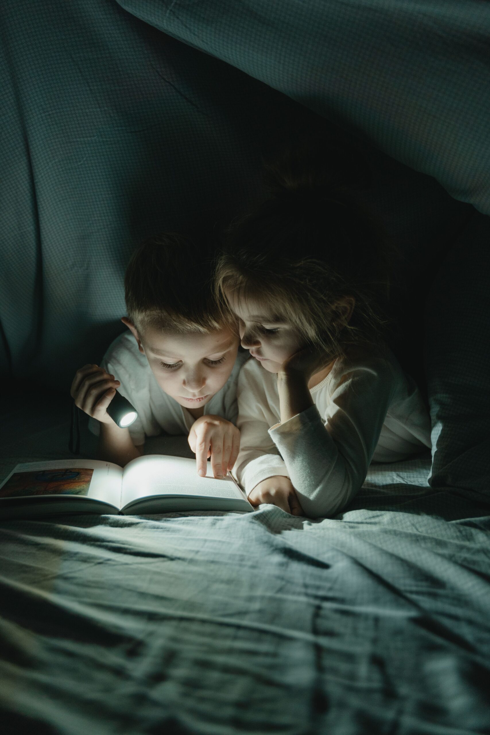 kids with flashlights reading under a sheet